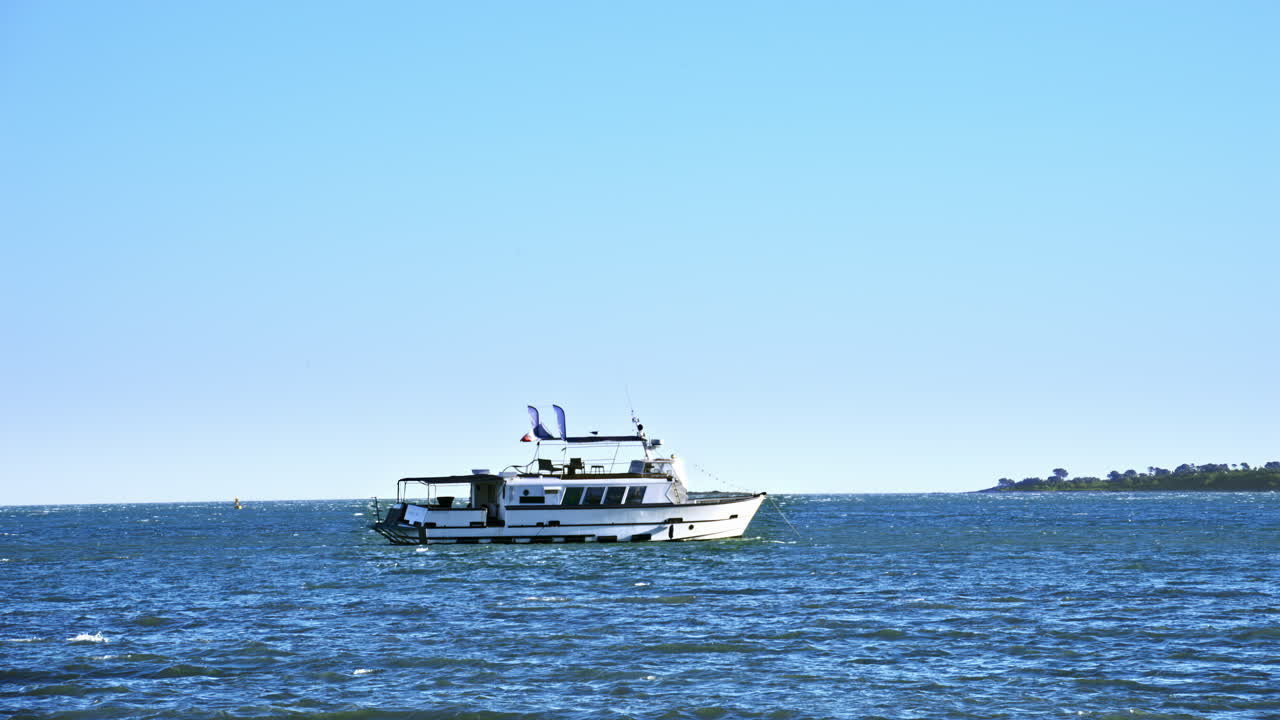 White boat with the flag of France on top moving on the sea with the blue sky on the background