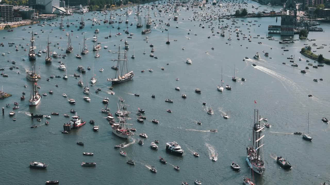 High panoramic establishing stationary drone tilted down over busy harbor during Amsterdam sailing event