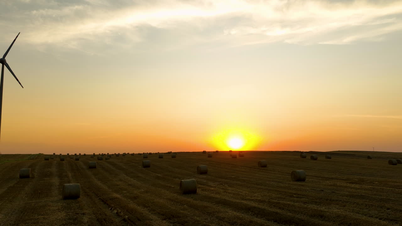 Wind turbine and round hay bales on farmland at sunset, clean energy and harvest season