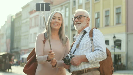 old couple standing together with a smartphone on the selfie stick and making a video or having videochat