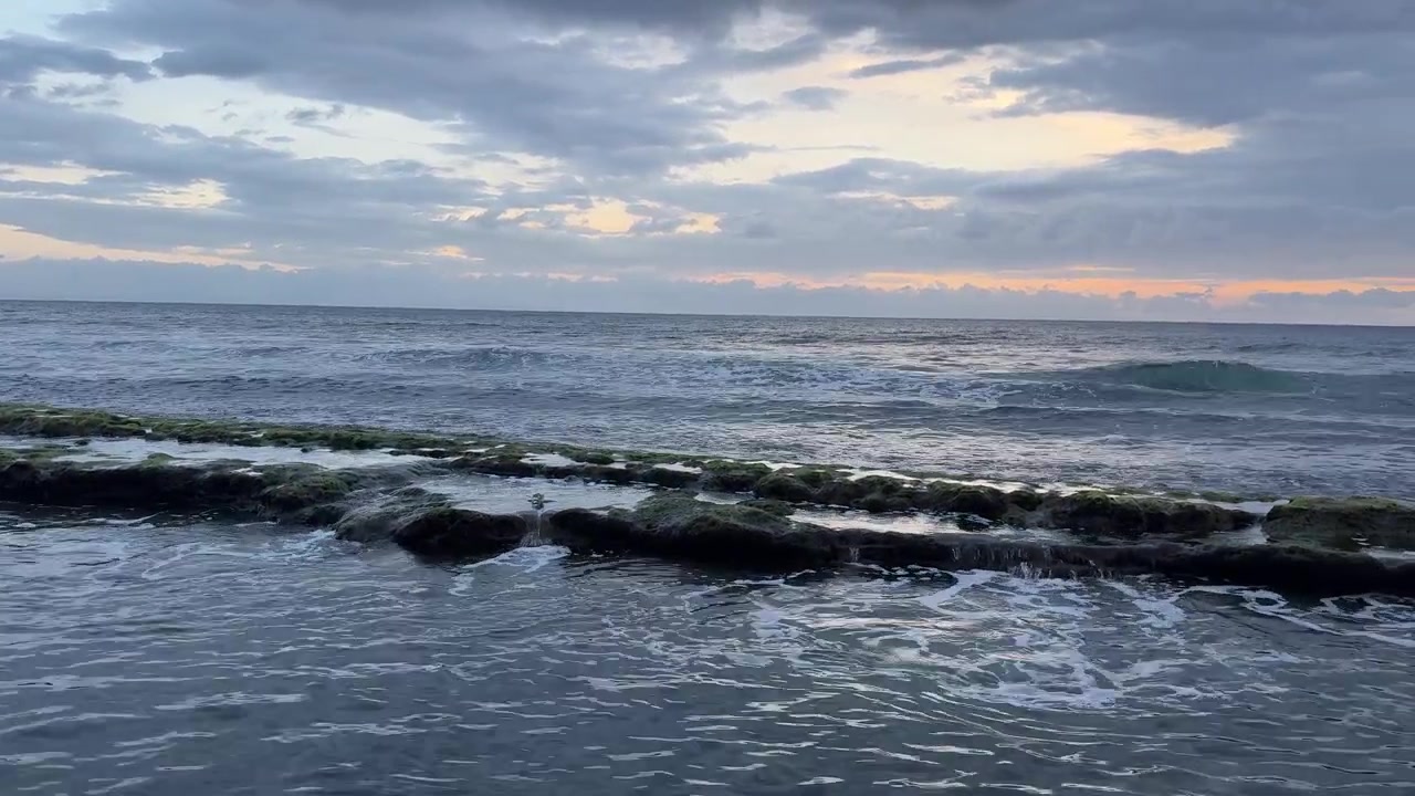 Onde che si infrangono su rocce muschiose su un sereno litorale oceanico al tramonto