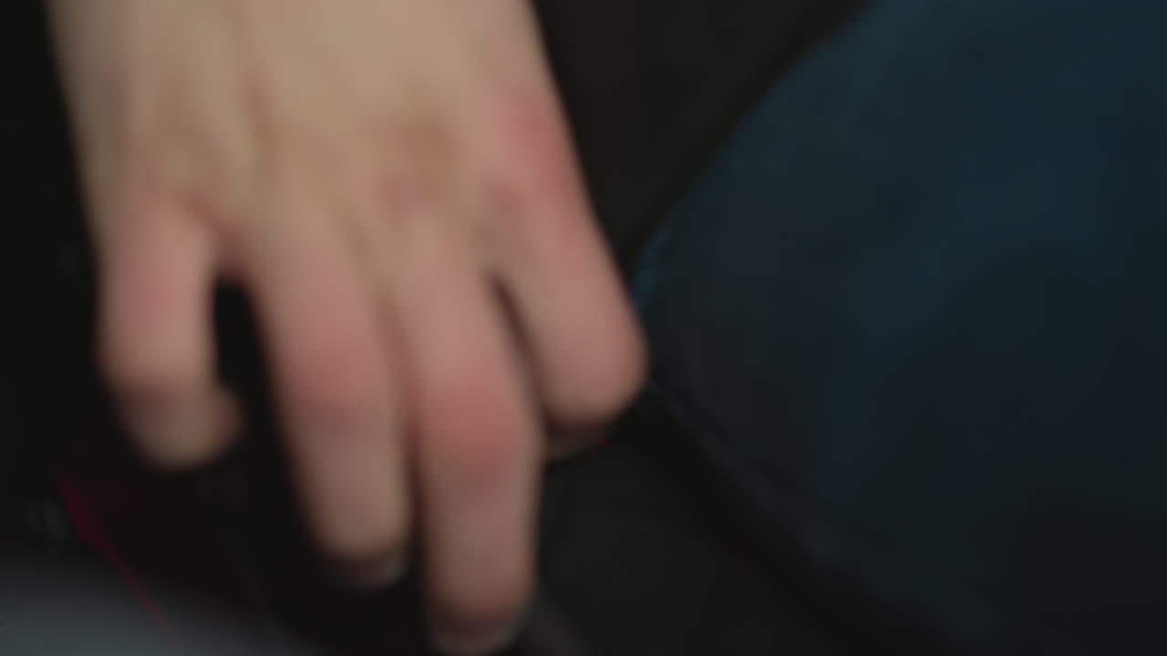 Close up of car owner hand locking seat belt in vehicle cabin beside fogged window wearing winter jacket focusing on finger pressing buckle latch amid ambient lighting highlighting safety gesture