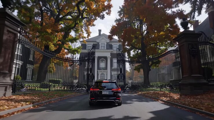 A video captures a rear view of a car driving through a tree-lined suburban street in autumn, shot