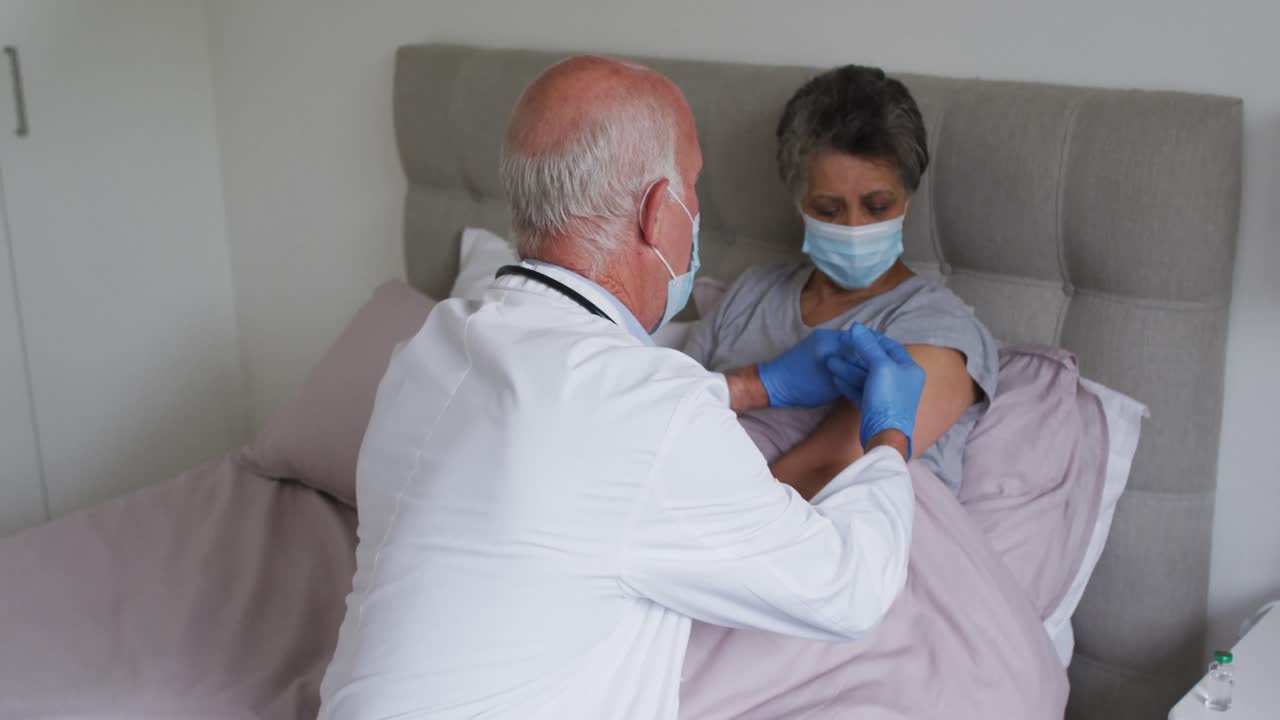 médico masculino caucásico vacunando a una mujer afroamericana mayor en casa