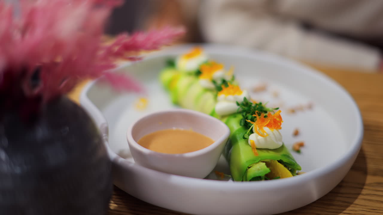 Close up of an avocado roll with sauce on a white plate at a restaurant
