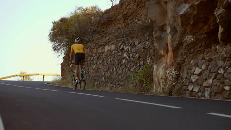 En-Cámara-Lenta,-El-Atleta-En-Bicicleta-Recorre-Una-Serpenteante-Montaña,-Deleitándose-Con-La-Cautivadora-Vista-De-La-Isla,-Personificando-Un-Estilo-De-Vida-Saludable.