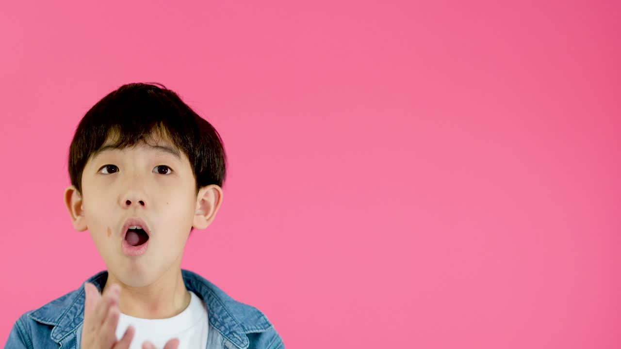 Young boy in denim jacket shouts with hands on face, bright pink background, studio lighting
