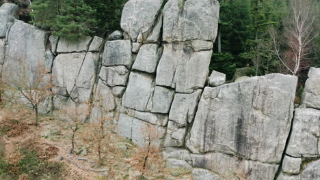 Giant-stone-wall-massif,-an-autumn-coniferous-forest-behind,-Czechia