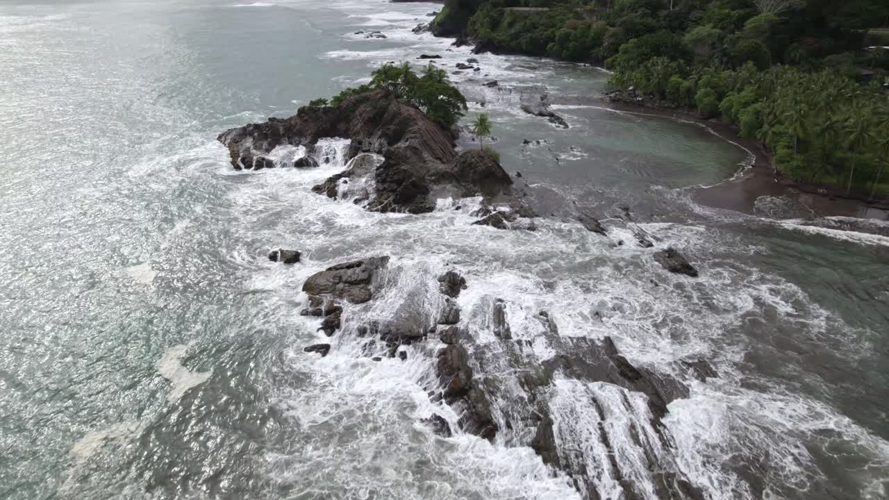 Aerial dolly in over rocky coastline and turquoise foamy waves near forest hillside in Dominicalito Beach, Costa Rica
