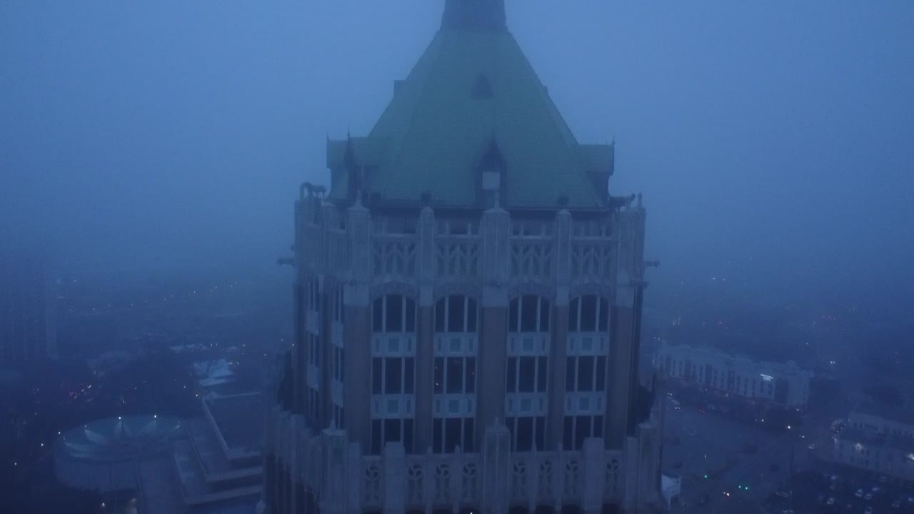 A gloomy drone shot unveils the American flag fluttering above the city, with gray skies and towering buildings in the background.