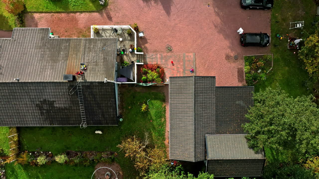 Aerial top view over a house and yard, person washing the roof, dog in the garden