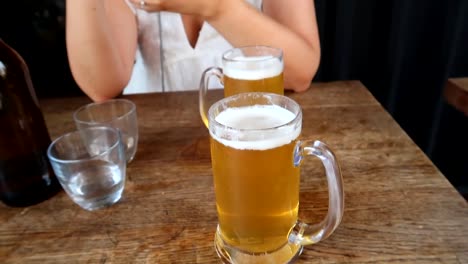 revealing shot of a young woman sitting at a table with two pints of beer in london