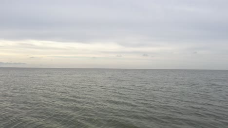 aerial: flying over water to horizon on a cloudy dull day