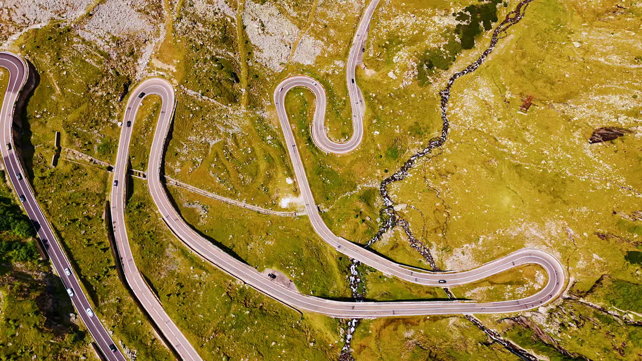 Amazing view on the valley crossed by the wavy road. Cars run by the Transfagarash highway in Romania. Aerial view
