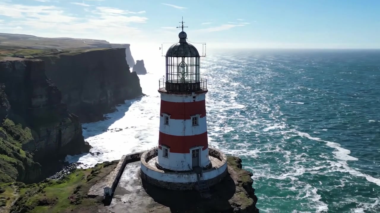 Splendide vedute aeree di un faro imponente posizionato su una maestosa scogliera che si affaccia su un oceano scintillante e un orizzonte sconfinato sotto un cielo limpido