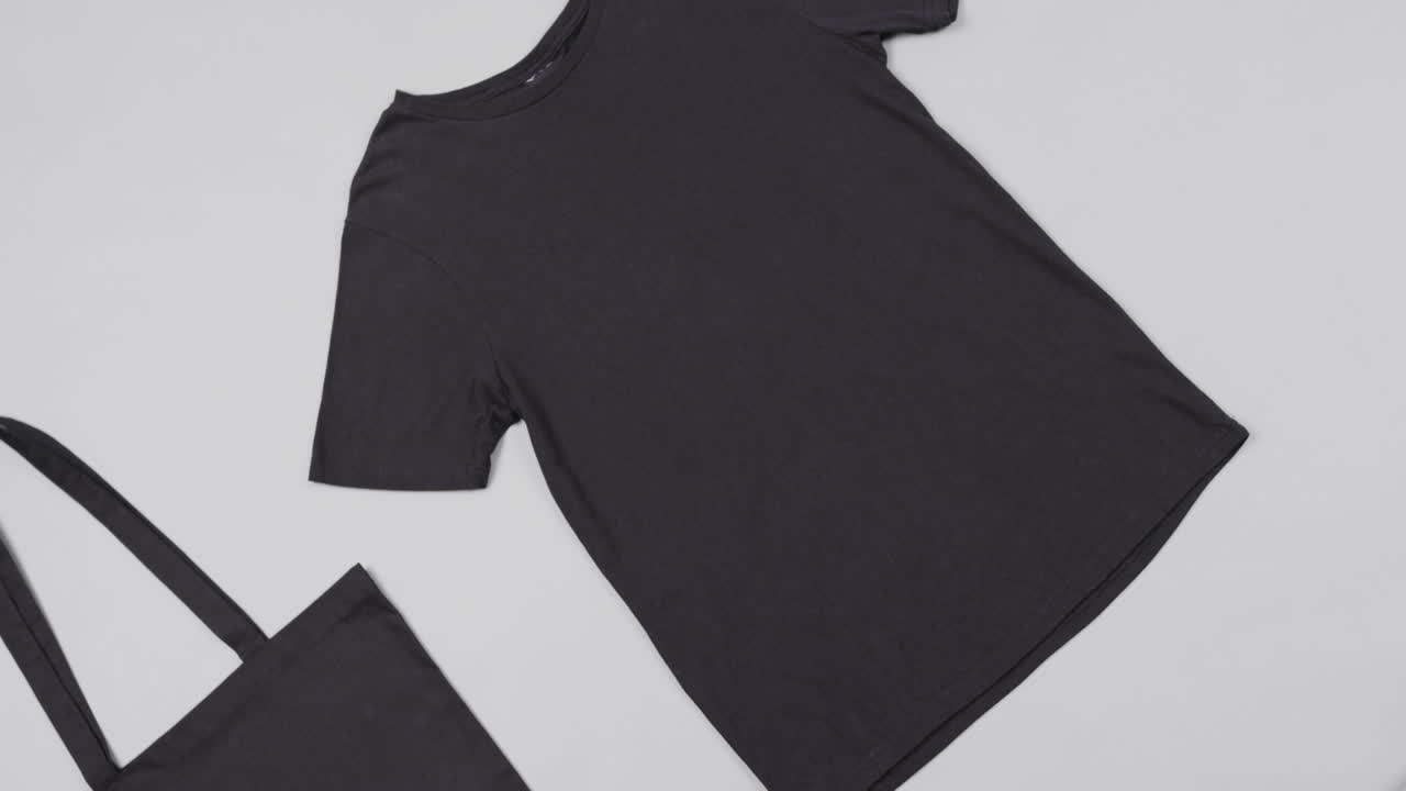 Close up of black bag and t-shirt on white background, with copy space, slow motion