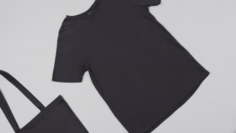primer plano de una bolsa negra y una camiseta sobre un fondo blanco, con espacio de copia, cámara lenta