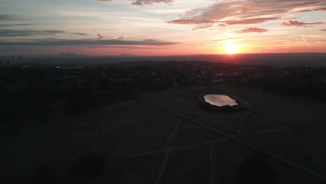 Aerial-shot-moving-forwards-over-Wimbledon-common-at-sunrise-with-London-skyline-in-background