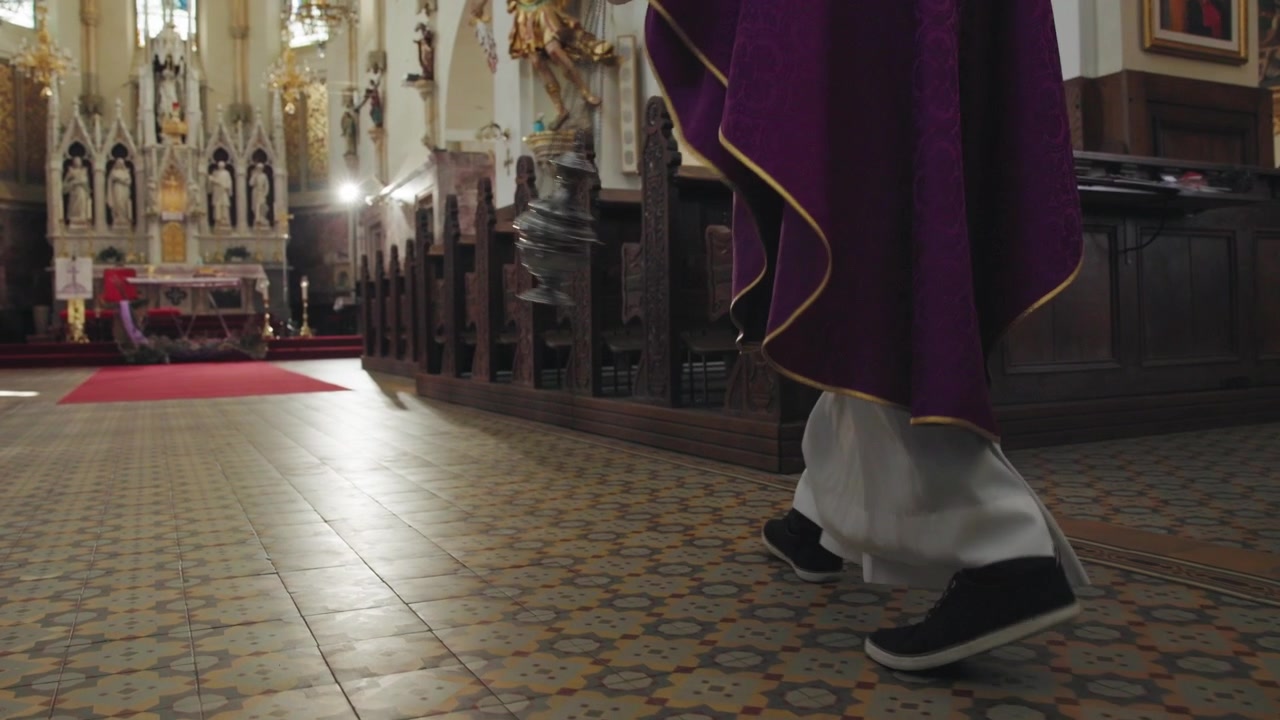 Sacerdote balançando um turíbulo fumegante pelo corredor em direção ao altar, um ritual litúrgico sagrado