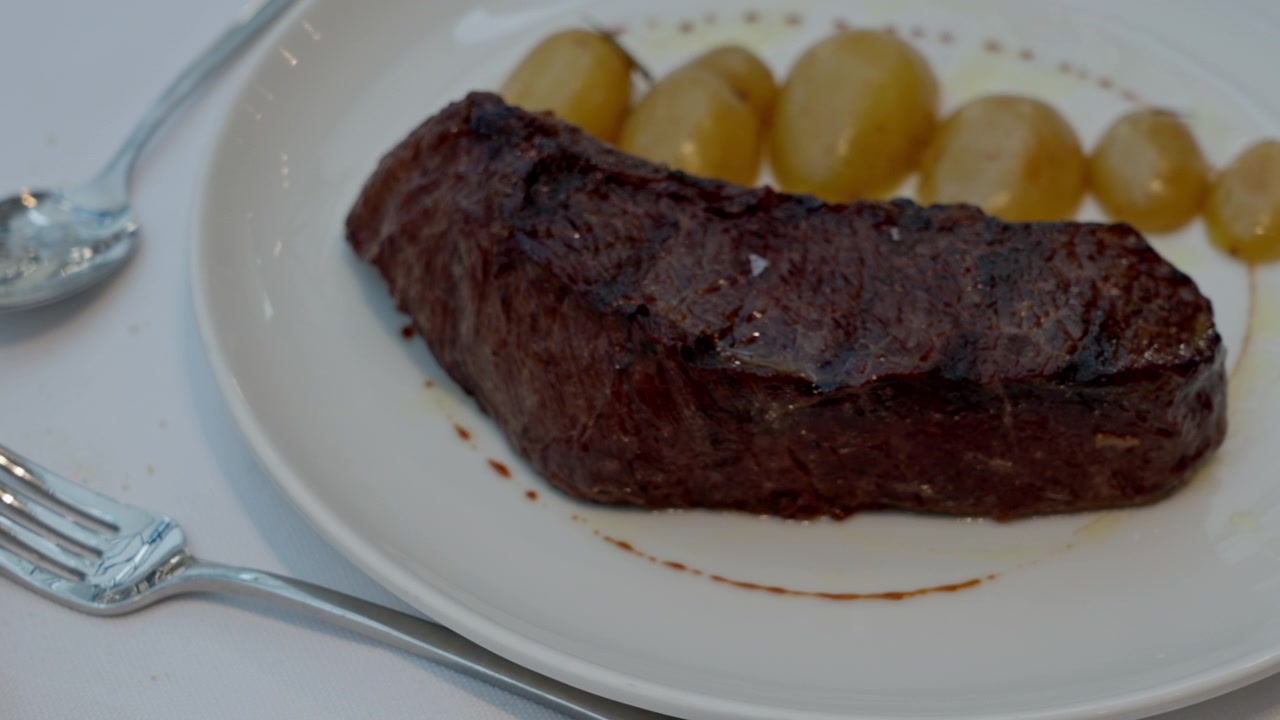 Bistecca alla griglia con patate croccanti presentata su un piatto bianco, pronta per essere gustata a un evento raffinato o a un incontro sociale