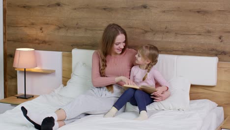 Joven-Madre-E-Hija-Hija-Acostada-En-La-Cama-En-Casa,-Leyendo-Cuentos-Antes-De-Dormir,-Cuentos-De-Hadas