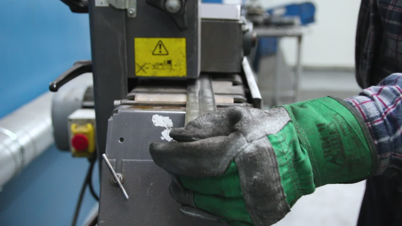 Sanding steel components in an advanced automatic grinder, worker in protective clothing and gloves