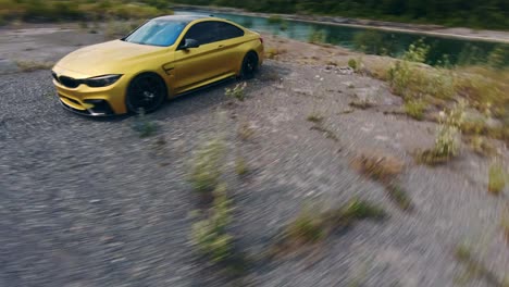 dron dando vueltas en círculos de un coche deportivo bmw de color dorado junto al borde del acantilado sobre el agua en una mina de piedra caliza abandonada