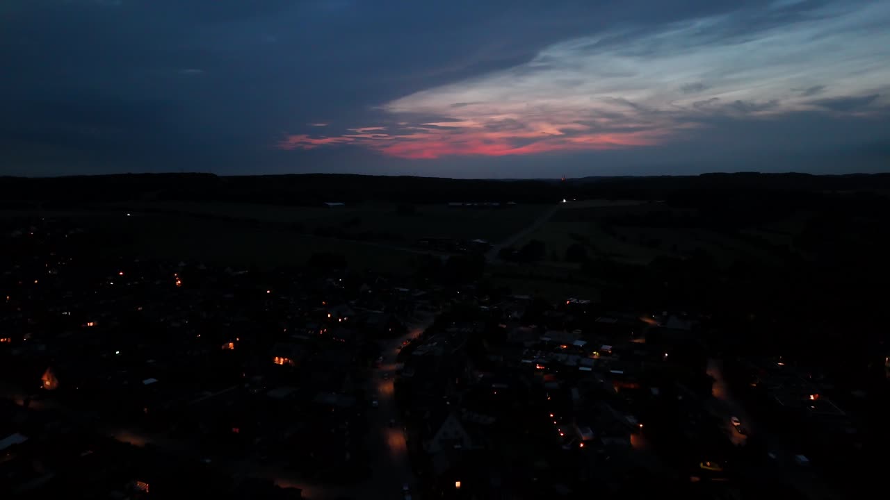 Golden sunset with pink sky at dusk- Lighting streets and roads with houses and homes in american town. Aerial forward wide shot. Night scene in suburbia.