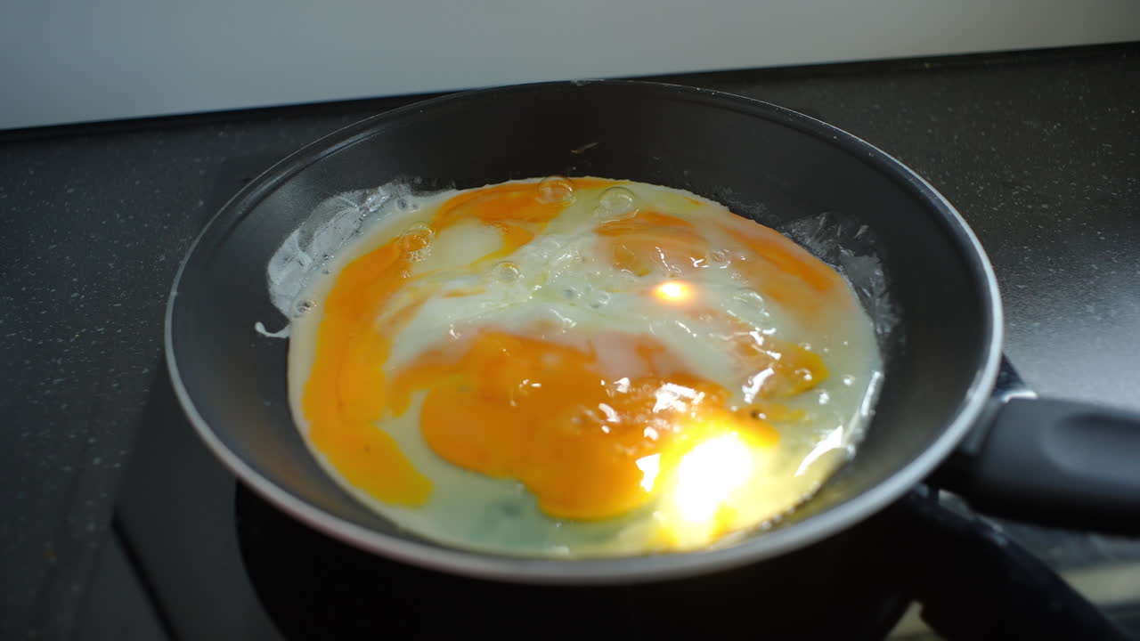 Professional chef carefully preparing sunny side up eggs, sizzling in cast iron pan over sleek black induction cooktop, showcasing precise culinary technique and fresh ingredient quality