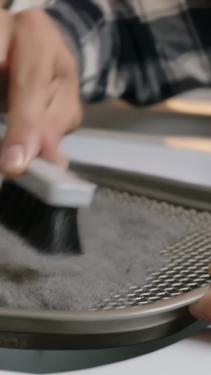 Vertical video: Placing brush on gray fabric on mesh at table, hand in plaid sleeve brushing lint