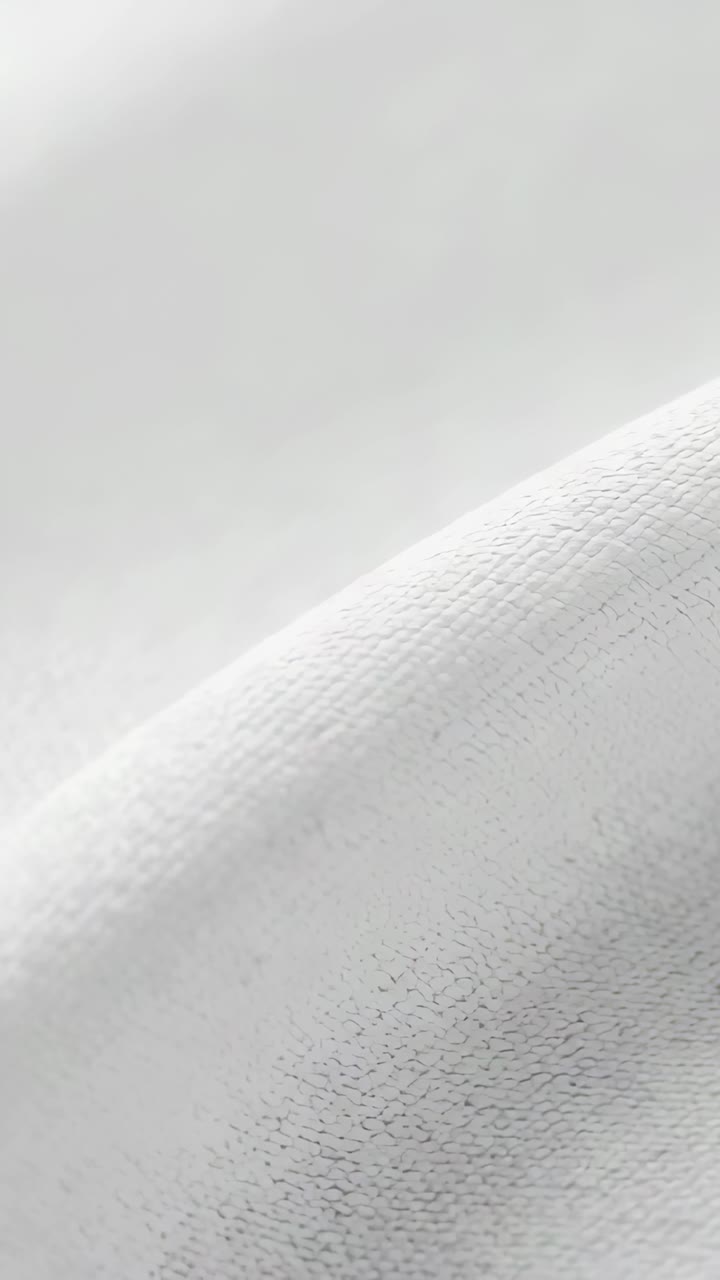 Vertical video: Sliding camera from closeup across white textile to reveal weave and diagonal folds