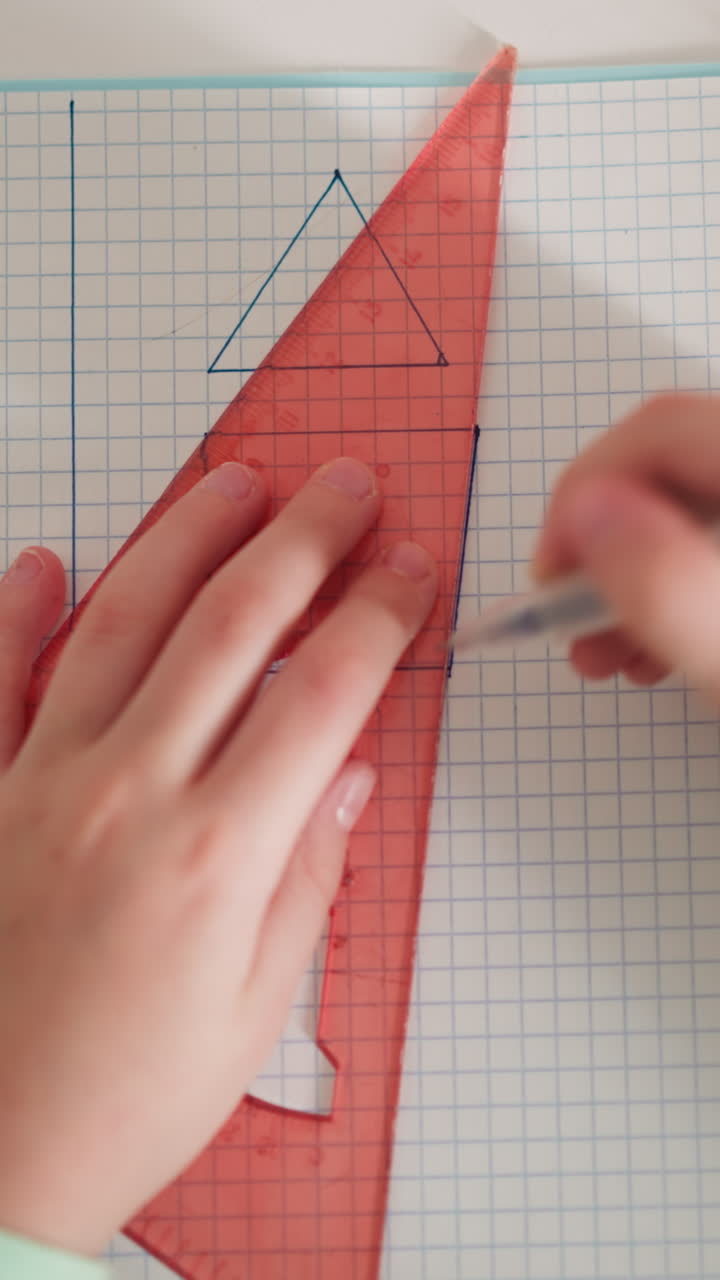 Little school student draws geometrical shape side with triangular ruler and gel pen on exercise book page at desk closeup. Pupil learns figures at lesson