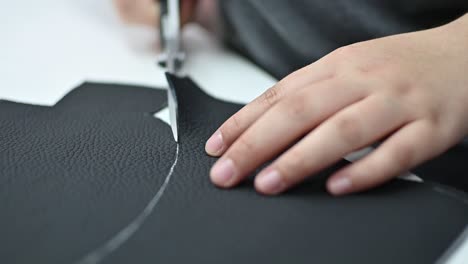 tailor cut black leather piece by white line, close up on hands in slow motion