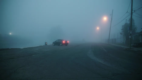 car parked in empty street covered with fog during dusk with low visibility glowing streetlights 4k