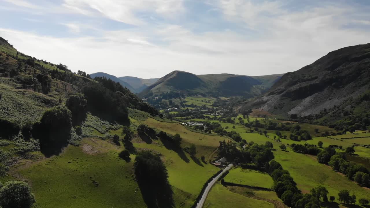 Aerial shot through the valleys in mid-Wales showing a beautiful valley with hills, fields and trees