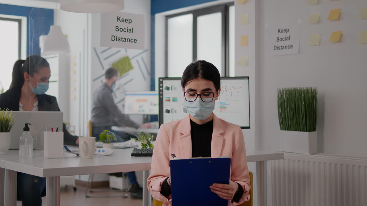 라이프 스타일 정보를 쓰는 동안 카메라를 바라보는 새로운 정상적인 사무실에 앉아있는 기업가