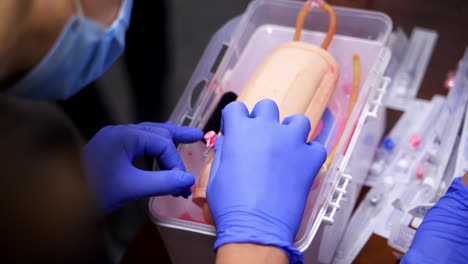 catheter insertion learning. students in sterile gloves study to put a catheter on a dummy hand. medical training. close-up.