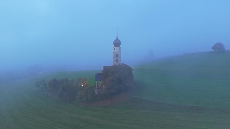 Naturskønt luftfoto af Sankt Valentin kirke med bjergtåge i Seis, Italien