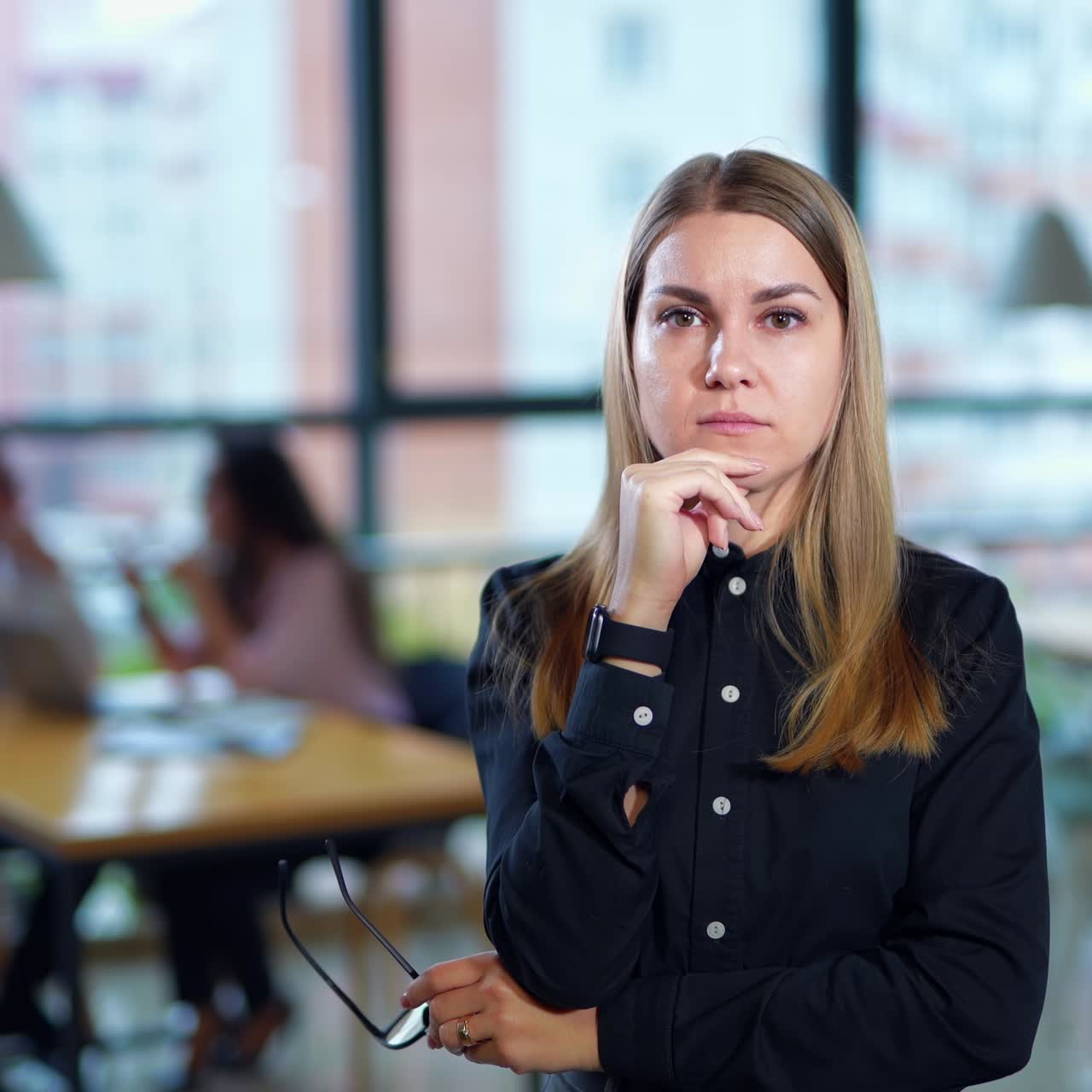 Young working lady feels headache and touching her forehead. Lady takes off her glasses and feels the nose bridge. Couple at table in blur at backdrop