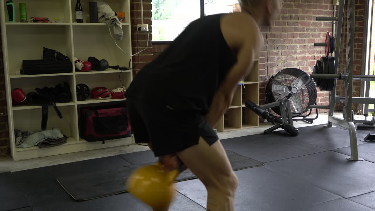 Tattooed man in home gym kettlebell swings
