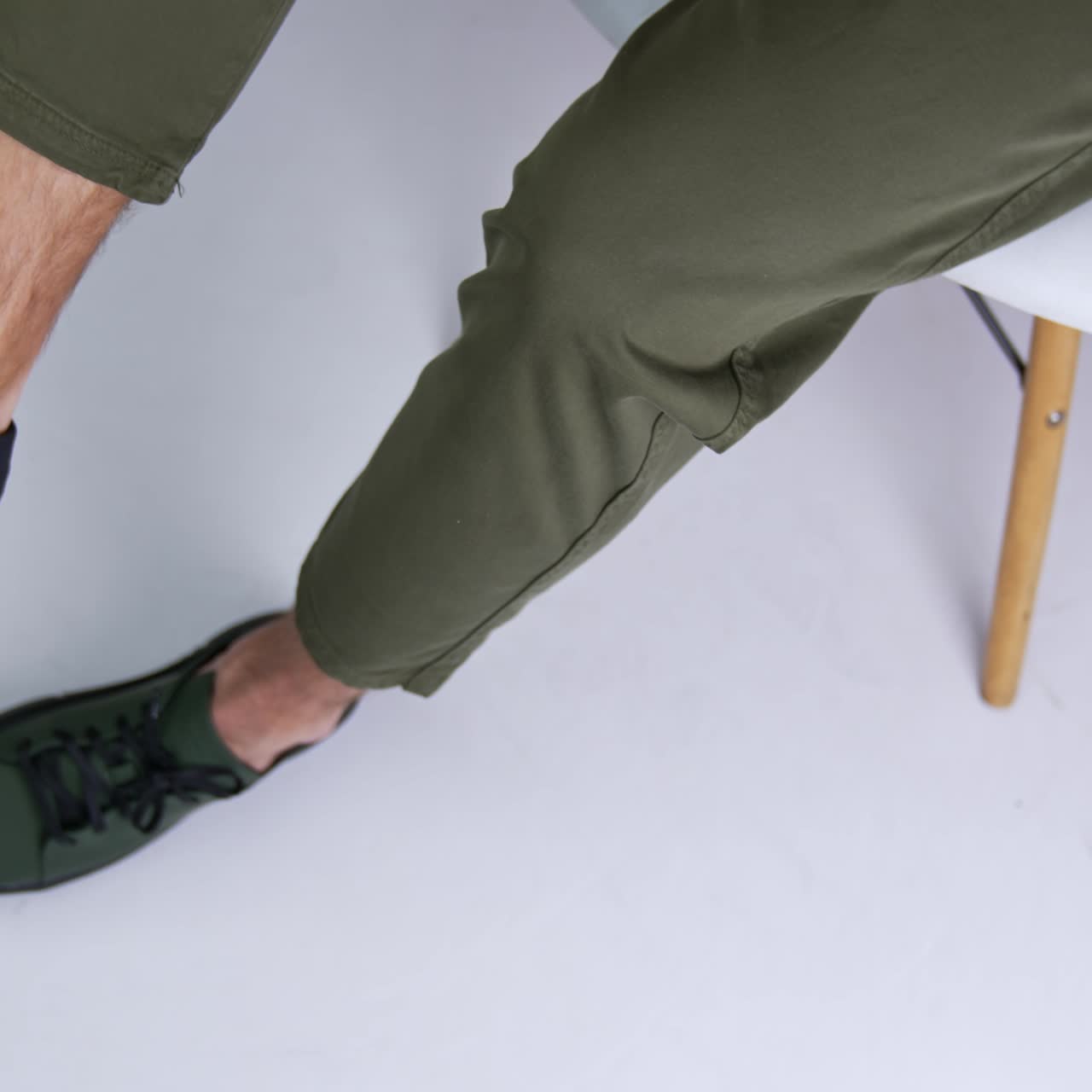 Man wearing dark green shoes with black laces and soles. Male sits on the chair putting leg on leg showing his footwear. Close up. Top view