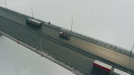 Lastwagen-Und-Autos-Fahren-Entlang-Der-Grauen-Brücke-über-Den-Zugefrorenen-Fluss