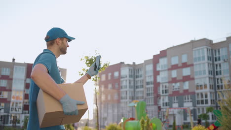 Un-Mensajero-Masculino-Está-Buscando-Un-Teléfono-Móvil-Para-Entregar-La-Dirección-De-Comida-De-Una-Tienda.-El-Repartidor-Navega-Por-Teléfono-En-La-Ciudad-Buscando-Direcciones-De-Entrega-De-Tiendas.-Entrega-Rápida