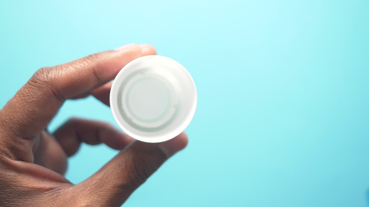 mano vertiendo líquido azul de una botella en una tapa blanca