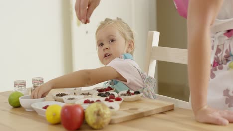 Child-watching-woman-sprinkle-candy-on-muffins