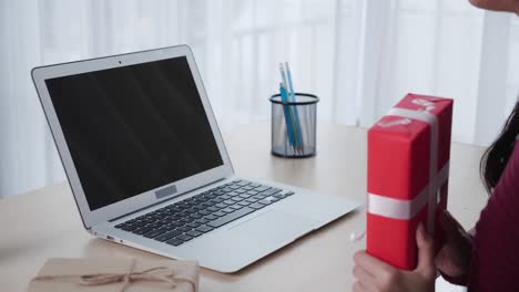 joven asiática llamada de video en línea con amigo y muestra caja de regalos en el día de navidad en computadora portátil con pantalla verde pantalla en blanco, distanciamiento social, nueva normalidad, concepto de comunicación.