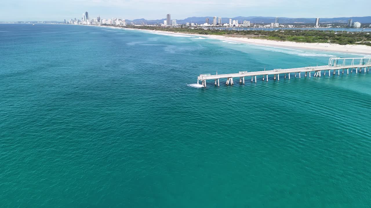 Aerial view of a man made pipe structure pumping water into the ocean close to a towering city skyline. Gold Coast Australia