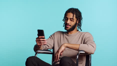 man in wheelchair chatting with friend over internet videocall using smartphone