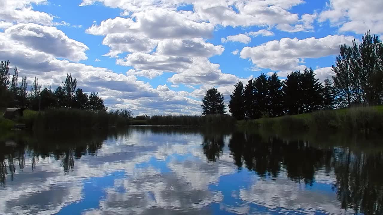 Vibrant blue lake water mirror reflection of bright clouds and trees in sky landscape
