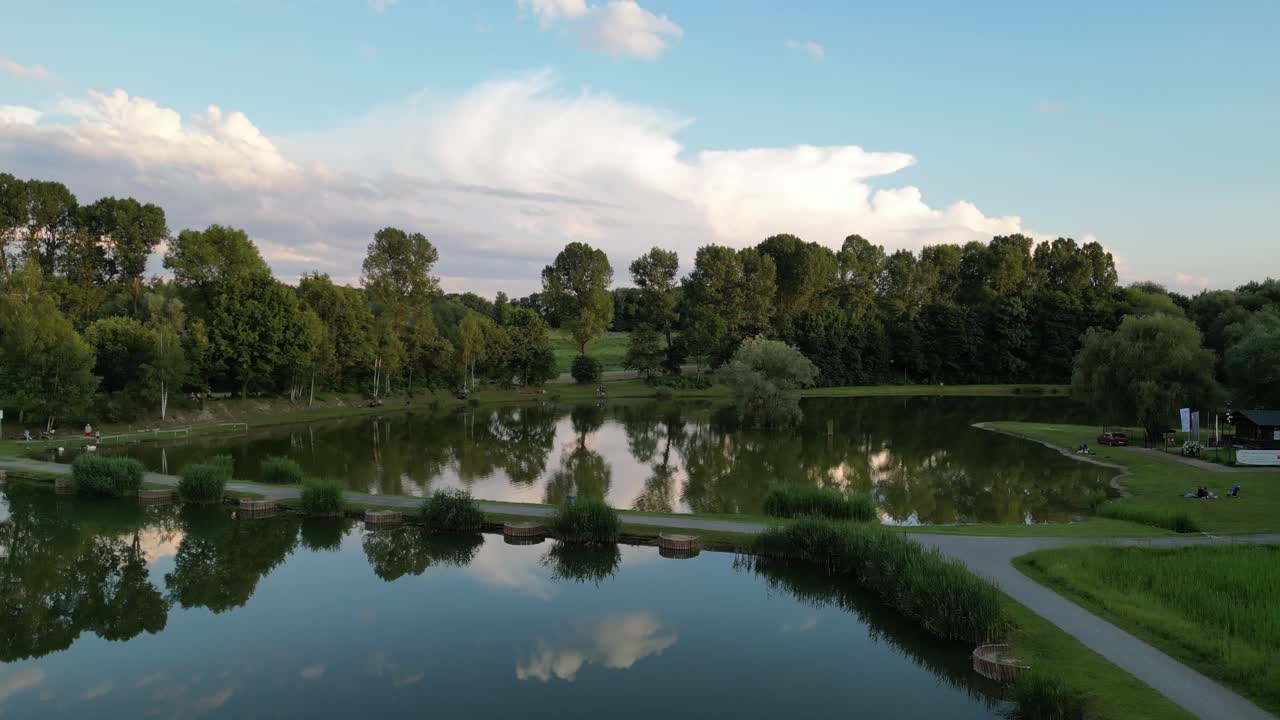 Small lake surrounded by greenery with sky reflecting in water - drone view 4K